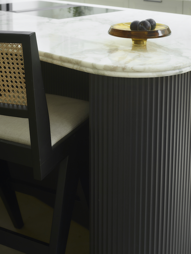 Close-up of a black fluted kitchen island with a rounded double bullnose stone worktop and integrated banquette seating.
