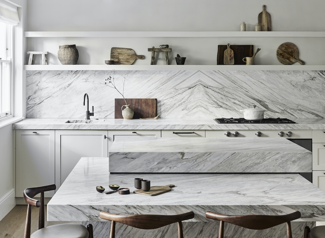 Statement marble kitchen island with layered stone worktops and waterfall edges in a bespoke white kitchen.