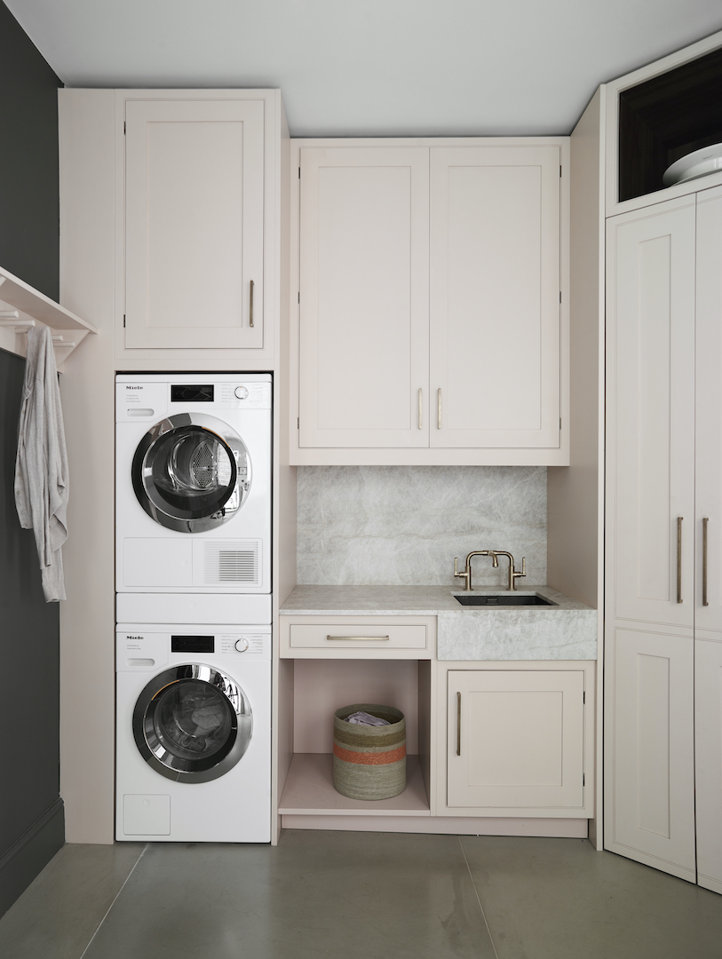 Bespoke bootility with painted light pink cabinetry, stacked laundry appliances, sink and floor-to-ceiling storage