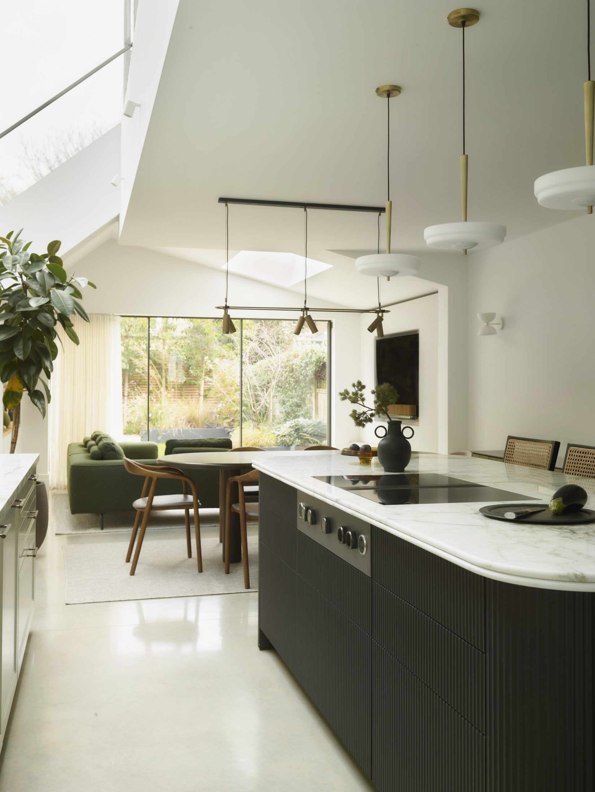 Bespoke kitchen with a curved fluted island, pale stone worktop and integrated banquette seating overlooking an open-plan dining area.
