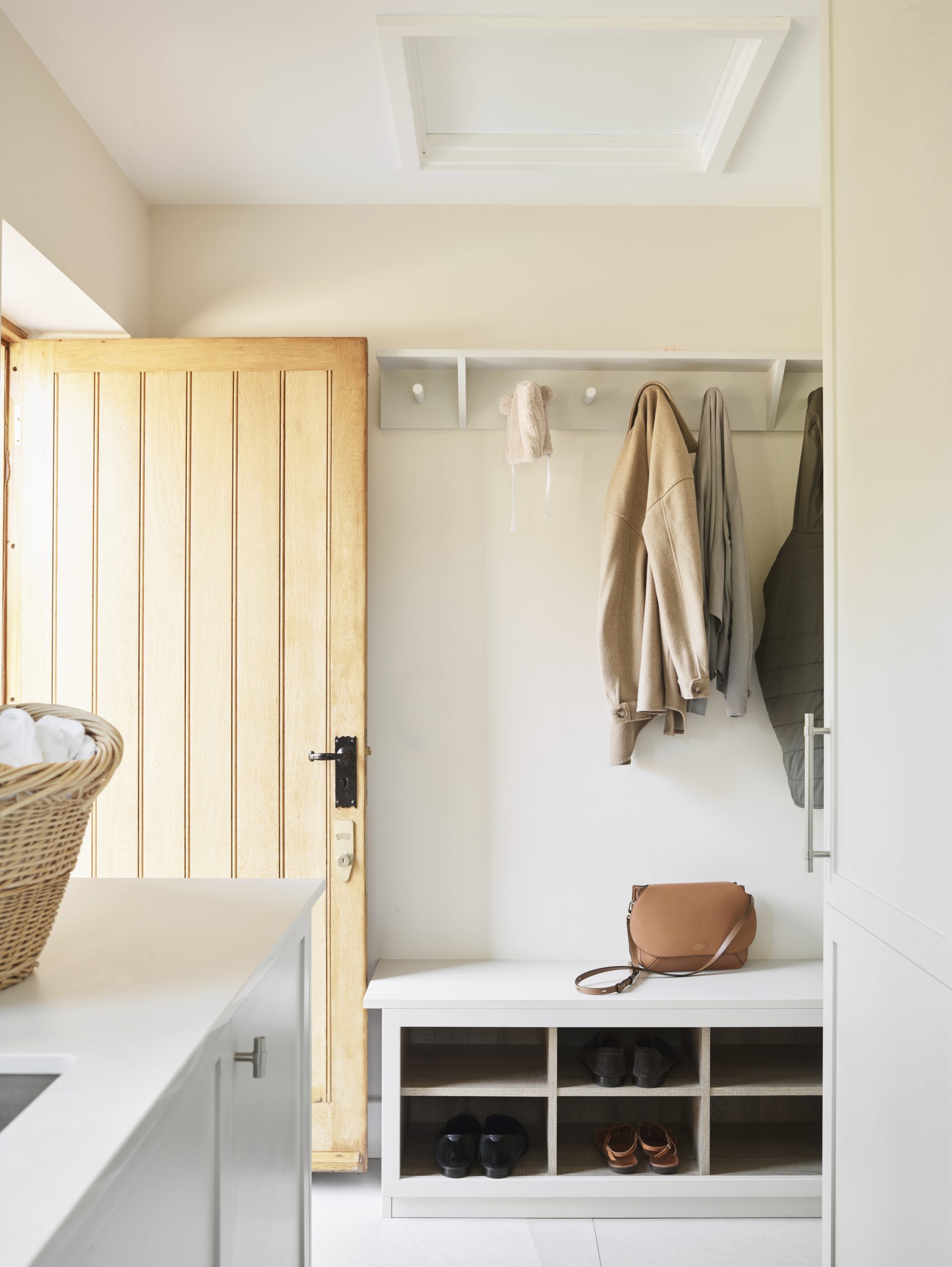 Light-filled boot room with built-in bench, open shoe storage, coat hooks and bespoke painted cabinetry