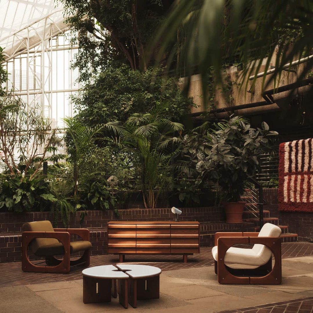 Mid-century-inspired timber furniture displayed among lush greenery in the Barbican Conservatory.