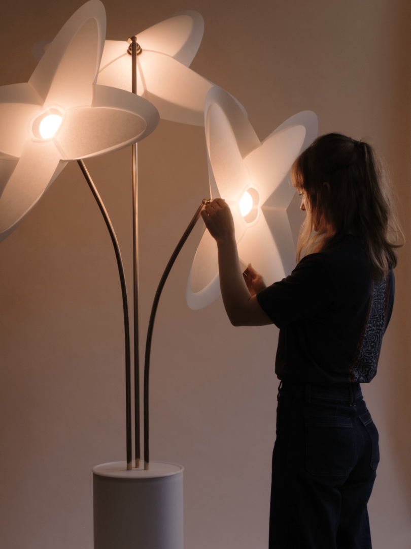 Designer adjusting a sculptural floor lamp with illuminated white petal-shaped shades and slender dark stems.