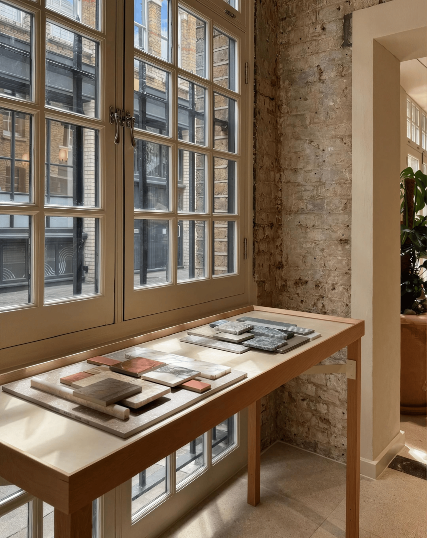 Natural stone and tile samples arranged on a timber display table beside large windows in a contemporary showroom.