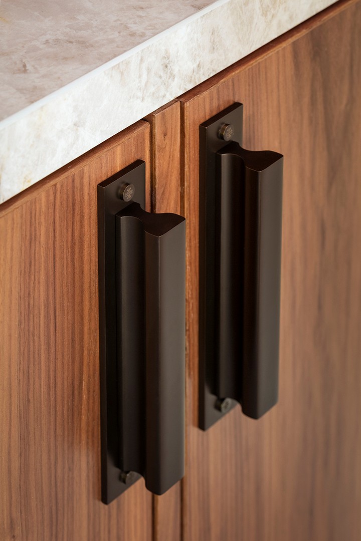 Close-up of two sculptural dark bronze cabinet handles fitted to richly grained timber cabinetry.