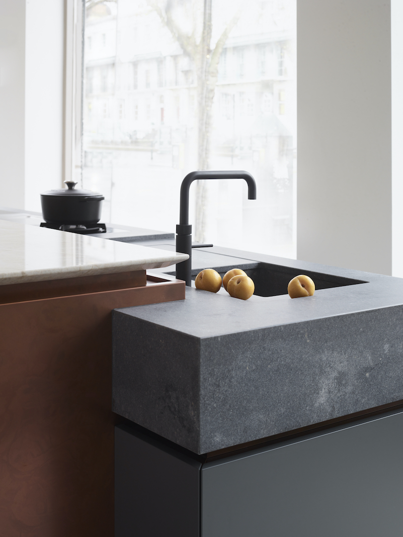 Close-up of a bespoke kitchen island in the Roundhouse Cheltenham showroom, showing a copper-wrapped base, dark stone sink and precisely detailed worktop edges.