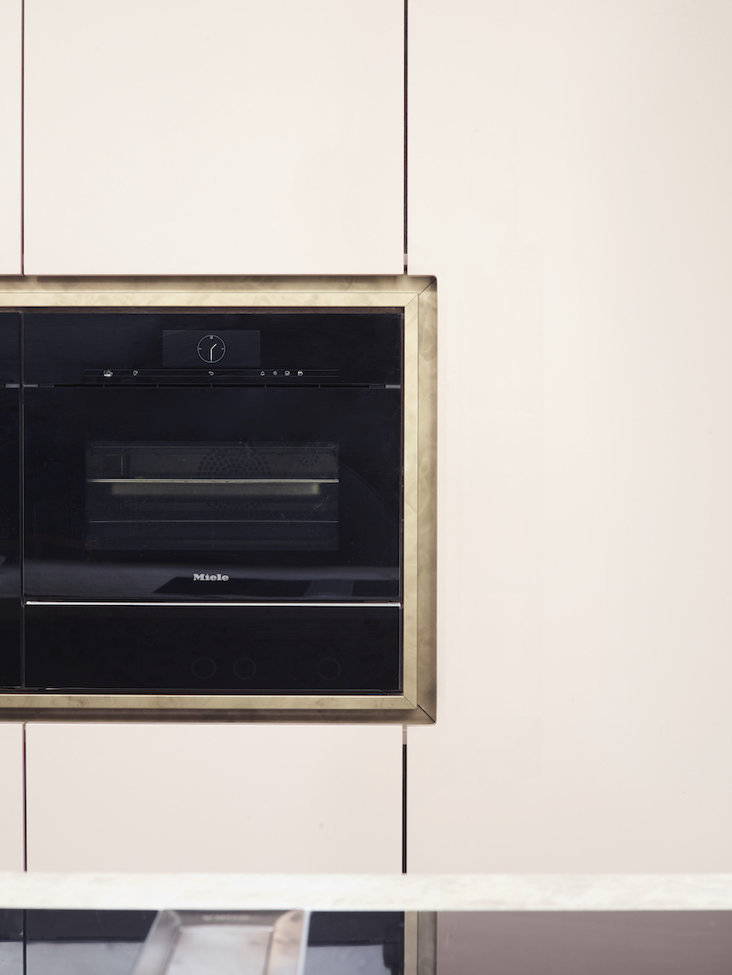 Built-in black oven framed by brass detailing within minimalist pale kitchen cabinetry, demonstrating seamless appliance integration in the Roundhouse Ali project.