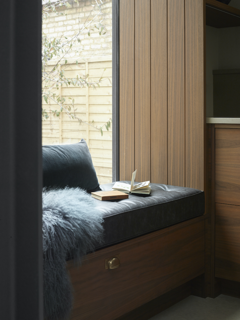Bespoke timber window seat with dark upholstered cushions, integrated storage and vertically grooved oak panelling in the Roundhouse Moony kitchen.