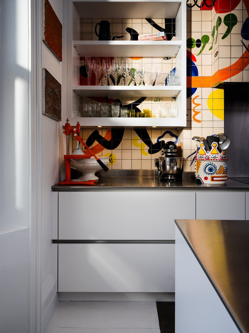 Bespoke Roundhouse kitchen storage with white open shelving, glassware, integrated appliances and colourful patterned tiles in Yotam Ottolenghi's home.