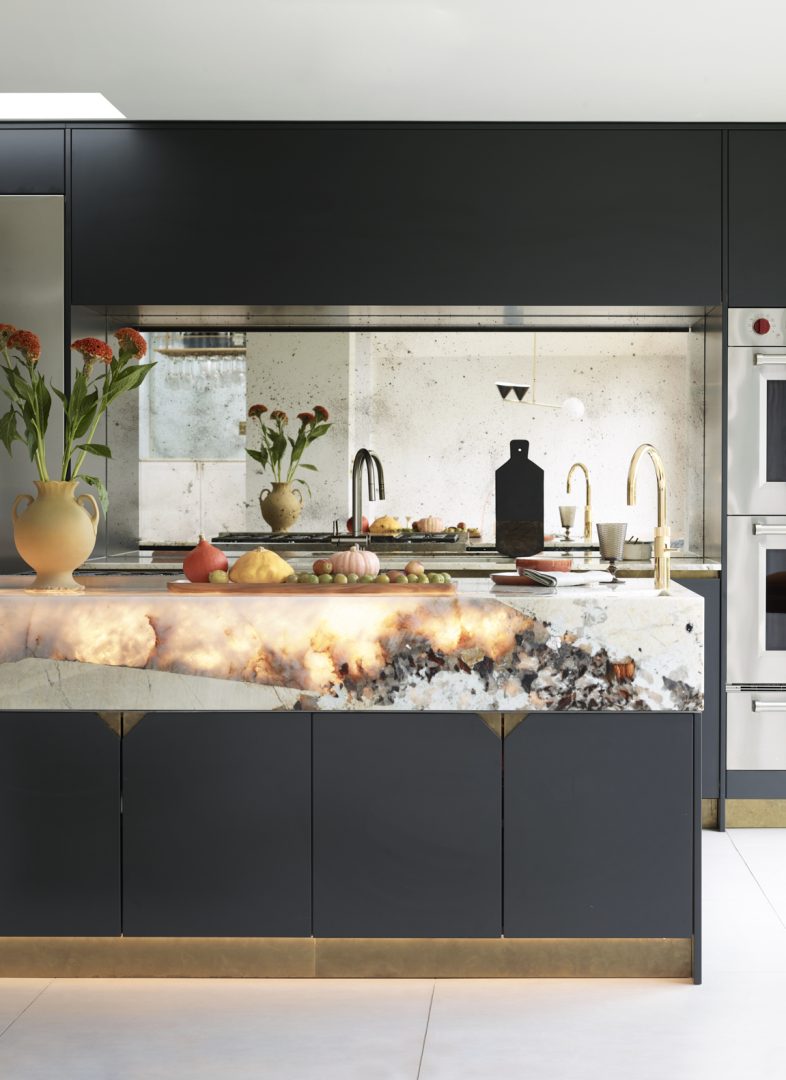 Contemporary kitchen with dark cabinetry, dramatic natural stone island, mirrored splashback and warm integrated lighting beneath the cabinetry.