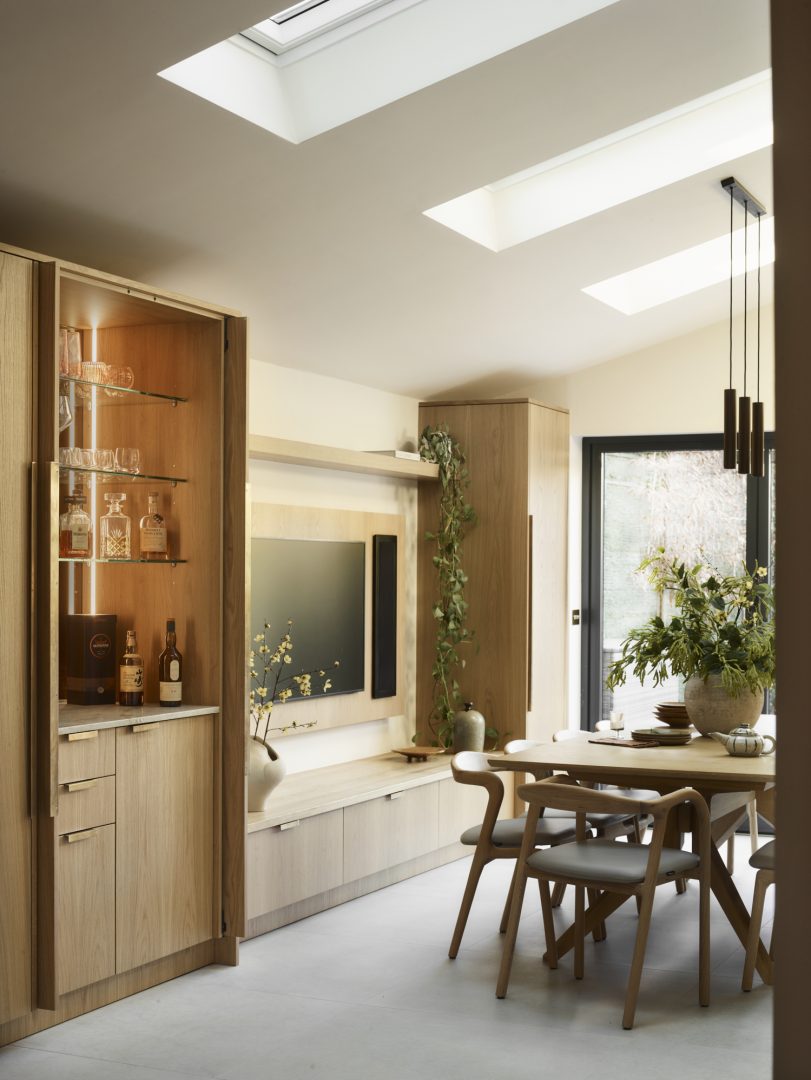 Bespoke oak joinery media unit with illuminated home bar with glass display shelving, integrated storage and natural timber finishes in the open-plan Roundhouse Bulpitt interior.