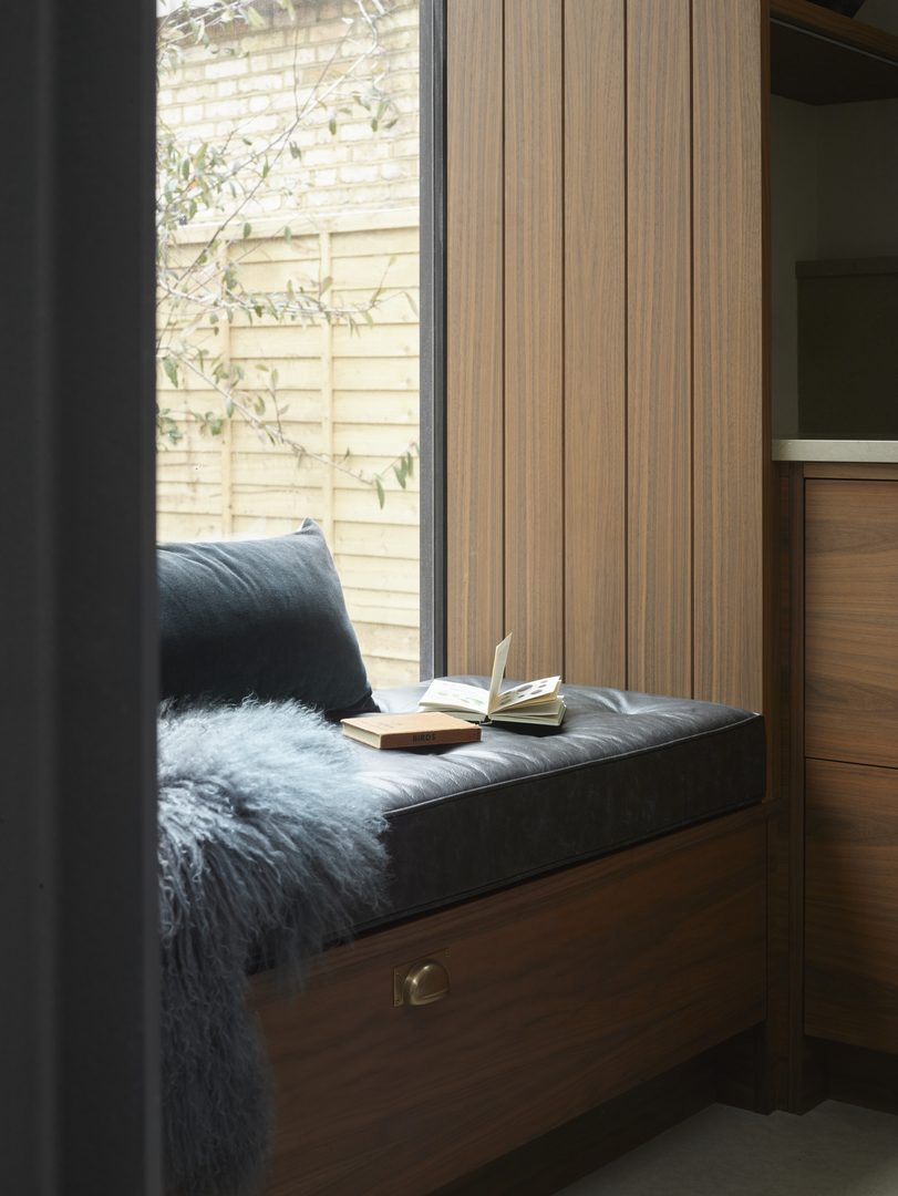 Bespoke walnut window seat with integrated drawer storage, deep blue cushions and garden views, creating a quiet seating area within the Moony kitchen.