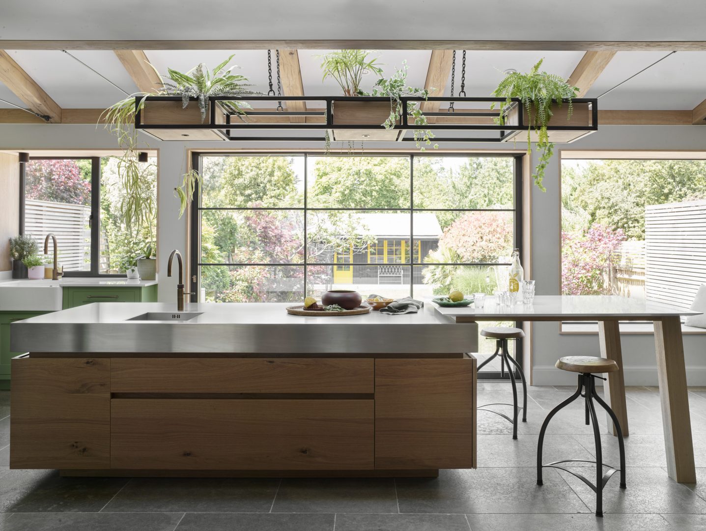 Natural oak kitchen island with stainless steel worktop, black-framed garden glazing and suspended greenery in Roundhouse's nature-inspired Oliver kitchen.